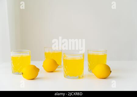 Ganze Zitronen in der Nähe von Gläsern mit reinem Zitronensaft auf grauem Hintergrund mit Kopierraum Stockfoto