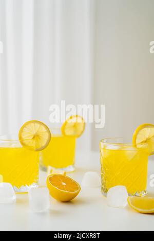 Natürliches Citrus Tonic und geschnittene Zitronen in der Nähe von Eiswürfeln auf grauem Hintergrund Stockfoto