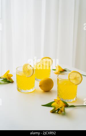 Frisches Zitrustonikum in der Nähe von Zitronen und gelbe Alstroemeria-Blüten auf weißem Hintergrund Stockfoto