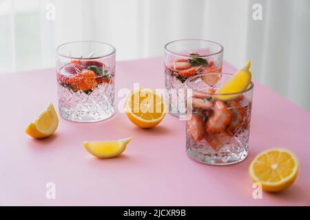 Frisches Tonic Water mit gehackten Erdbeeren in der Nähe geschnittenen Zitronen auf weißer Tischplatte Stockfoto