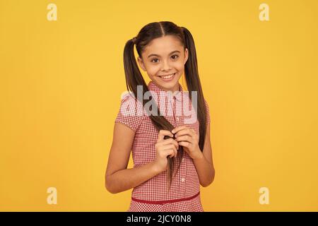 Glauben Sie an Schönheit. Schüchternes Mädchen gelber Hintergrund. Kind mit schüchternem Lächeln berühren die Haare Stockfoto