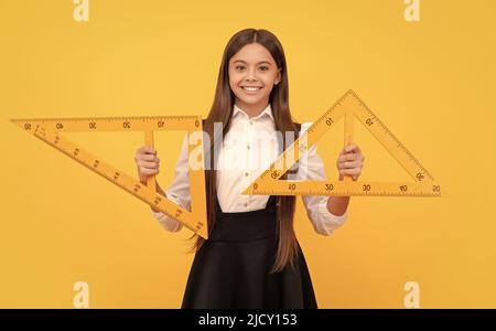 Lächelndes Teenager-Mädchen halten Dreieck. Zurück zur Schule. Algebra und Geometrie. Kind Mathematik lernen. Stockfoto