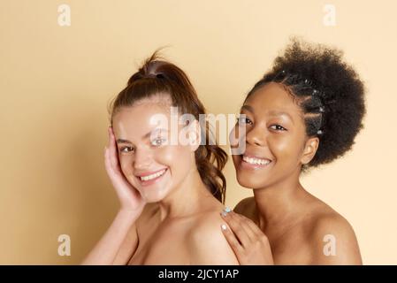Porträt zweier wunderbarer multiethnischer Frauen auf beigem Hintergrund. Schöne Frauen, makellose Haut. Diverse Freunde Stockfoto