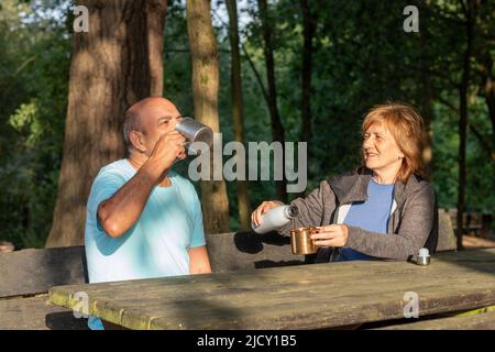 Mann und Frau sitzen auf einer Bank, die nach dem Trekking in den Bergen mit Wasser in einem Metallbecher versorgt werden Stockfoto