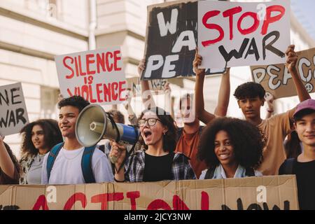 Gruppe multikultureller Jugendaktivisten, die in den Straßen der Stadt gegen Krieg und Gewalt protestieren. Demonstranten der Generation Z rufen Slogans und Rais Stockfoto