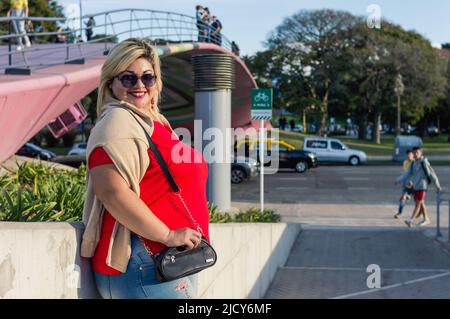 Schöne junge kaukasische plus Größe lateinische argentinische Frau in rot und Sonnenbrille, stand bei Sonnenuntergang in buenos aires Stadt lächelnd Blick auf die kam Stockfoto