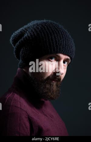 Dramatisches Porträt von Millennial in schwarzem Strickmütze und Pullover auf dunklem Hintergrund Stockfoto