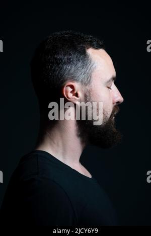 Dramatisches Porträt-Profil von tausendjährigen bärtigen Kerl auf schwarzem Hintergrund Stockfoto