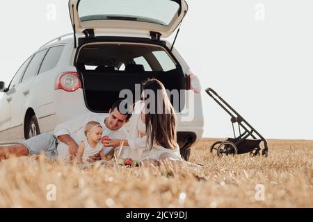 Junge Familie mit Kleinkind Kind genießen Picknick außerhalb der Stadt, Mama und Papa mit ihrer Tochter Spaß Zeit auf dem Feld während Weekend Road Stockfoto