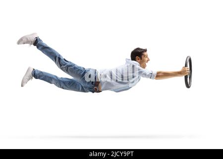 Ganzkörperaufnahme eines aufgeregten jungen Mannes, der auf weißem Hintergrund ein isoliertes Lenkrad hält und fliegt Stockfoto
