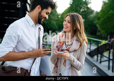 Glückliche junge Geschäftsleute, die im Freien chatten und digitale Geräte nutzen Stockfoto