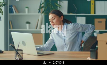 Office-Syndrom.Frau, die versucht, vom Tisch plötzlich Schmerzen im Rücken fühlen.Frau, die sich müde von langen sitzenden Lebensstil Versuchen Sie, sich zu entspannen und R Stockfoto