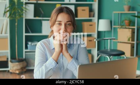 Porträt einer glücklichen jungen Frau, die an ihrem Schreibtisch im Büro sitzt. Erfolg und Geschäftskonzept. Büroangestellter. Stockfoto