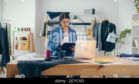 Ein professioneller Modedesigner erstellt in einem Fashion Business Startup Studio eine neue Kollektion, zeichnet, arbeitet mit Skizzen mit einem Laptop. Konzept von H Stockfoto