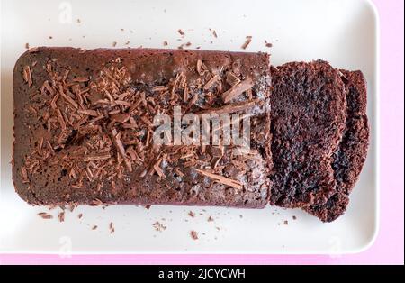 Ein reicher köstlicher vierfach-Schokoladenkuchen, frisch gebacken und auf einem Teller gesessen. Zwei Scheiben haben aber geschnitten zeigt die feuchte Schokolade Mitte Stockfoto