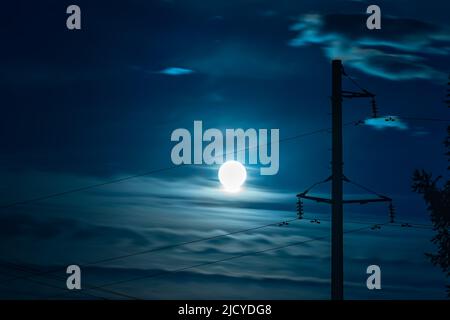 Blick auf den hellen Mondkreis bei Vollmond an einem wolkigen Nachthimmel vor dem Hintergrund elektrischer Drähte mit leerem Textraum Stockfoto