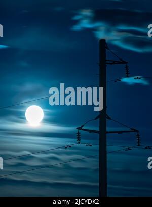 Blick auf den hellen Mondkreis auf einem Vollmond in einem bewölkten Nachthimmel vor dem Hintergrund von elektrischen Drähten und einem Holzmast einer Stromleitung Stockfoto