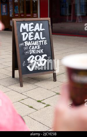 Ein Sandwich-Schild in einem britischen Einkaufsviertel, auf dem ein günstiges Angebot für eine Mahlzeit in einer nahegelegenen Bäckerei steht. Das Angebot umfasst ein Getränk, Kuchen und Baguette Stockfoto