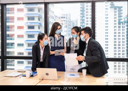 Multiethnisches Geschäftsteam mit Gesichtsmaske während eines Geschäftstreffens in einem neuen normalen Büro. Verschiedene Unternehmenskollegen Brainstorming mit Technologie d Stockfoto