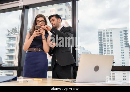 Junger kaukasischer Partner hält Smartphone und diskutiert im modernen Büro über Geschäfte Stockfoto