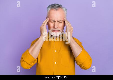 Foto von traurigen alten grauen Frisur Mann Hände Kopf tragen Senf Hemd isoliert auf violettem Hintergrund Stockfoto