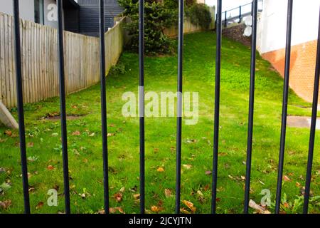 Schwarzes Eisengeländer mit gemähtem Gras hinten und einem Holzzaun Stockfoto