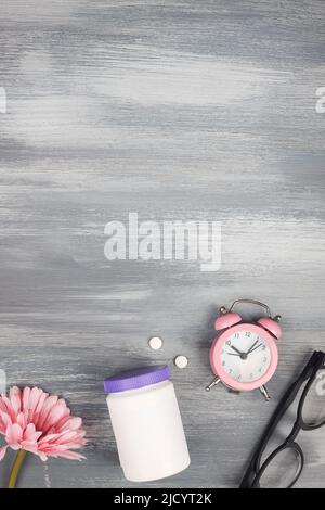 Frauen Gesundheitskonzept. Medizin, Gesundheitsstil. Kopierraum. Weiße Plastikflasche mit Pillen, Blumen, Gläser und Uhr auf blauem Holzhintergrund. Stockfoto