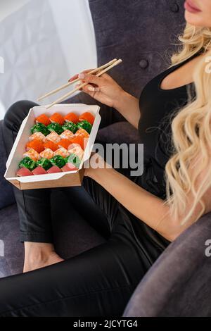Essen von Sushi mit Essstäbchen aus der Nähe, Essen zum Mitnehmen und Lieferservice, Lachs-Sushi-Brötchen, leckeres Essen, Sushi-Lieferung. Stockfoto