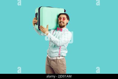 Hübscher, eleganter junger Mann, der Koffer auf seinen Schultern auf hellblauem Hintergrund hält. Stockfoto