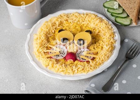 Tolles Essen für Kinder zum Frühstück - süßer Löwenkopf aus Rührei, Käse, Radieschen und schwarzen Oliven auf weißem Teller Stockfoto