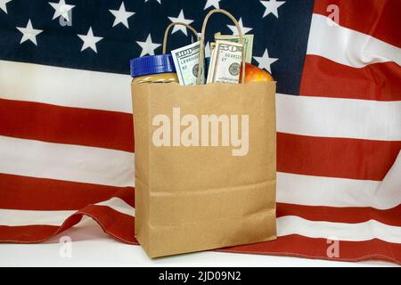 Eine einfache braune Papiertüte, gefüllt mit Lebensmitteln und Geld auf einer amerikanischen Flagge Stockfoto