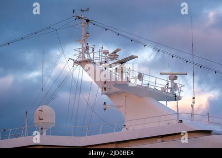 Helsinki / Finnland - 16. JUNI 2022: Nahaufnahme eines Radarmastes eines Schiffes gegen dunkle Sturmwolken während des Sonnenuntergangs Stockfoto