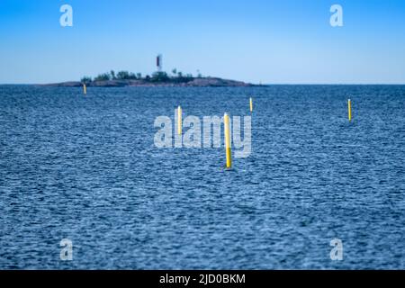 Helsinki / Finnland - 15. JUNI 2022: Eine Reihe von gelben Navigationsbojen, die auf dem Wasser schweben. Eine kleine Insel im Hintergrund. Stockfoto