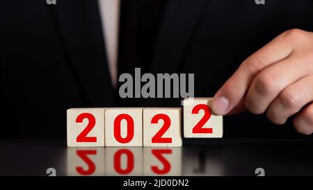 Mann Hand Flipping Würfel mit Jahr 2021 bis 2022. Neujahr Konzept. Copy space. Hand hält Holzwürfel mit Klappblock 2021 bis 2022 Wort auf dem Tisch Stockfoto