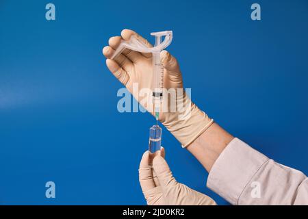 Behandschuhte Hand halten Sie die Spritze auf blauem Hintergrund Stockfoto