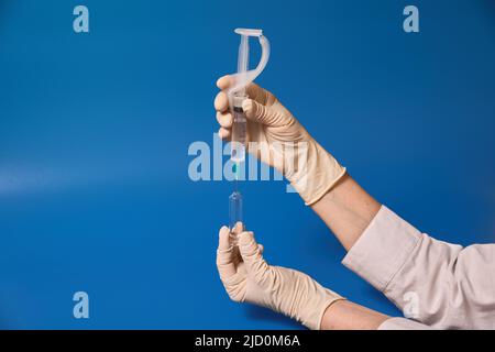 Behandschuhte Hand halten Sie die Spritze auf blauem Hintergrund Stockfoto