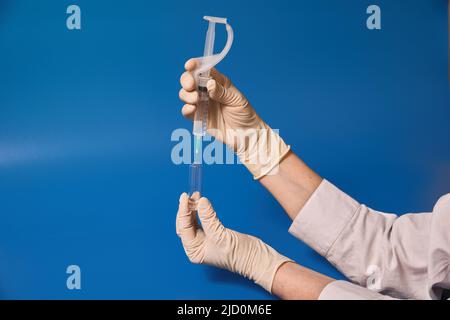 Behandschuhte Hand halten Sie die Spritze auf blauem Hintergrund Stockfoto