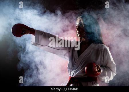 Schönes Mädchen Ausübung Karate Punch vor rotem Nebel Hintergrund Stockfoto