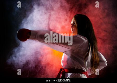 Schönes Mädchen Ausübung Karate Punch vor rotem Nebel Hintergrund Stockfoto