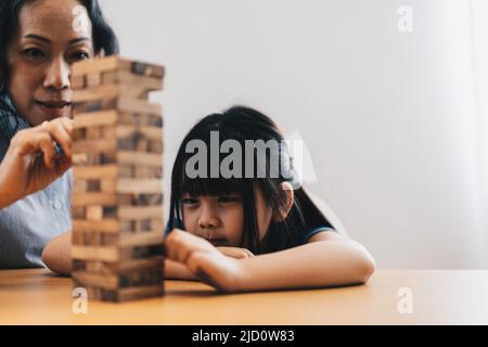 Glückliche Momente der asiatischen Großmutter mit ihrer Enkelin, die Holzkonstruktor spielt. Freizeitaktivitäten für Kinder zu Hause. Stockfoto