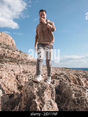 Der junge Mann springt auf einem Wüstenboden vor dem Berg Cape Greco Stockfoto