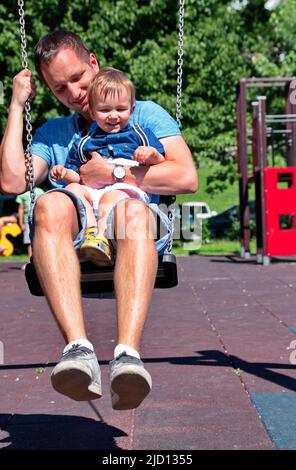 Vater schwingt mit seinem kleinen Jungen auf dem Spielplatz Stockfoto