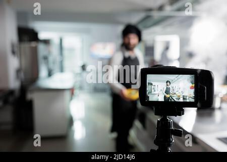 Nahaufnahme der Kamera Aufnahme Chefkoch Kochen köstliche feine Speisen in der Restaurantküche für kulinarische Kurs. Kochen Sie die Zutaten für eine leckere Mahlzeit, während Sie die Show für das Fernsehprogramm Filmen Stockfoto