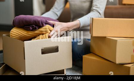 Eine Frau, die einen Karton mit einer gefalteten Kleidung hält. Weibliche Auspacken ihrer Versandkarton. Stockfoto