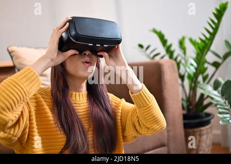 Eine begeisterte und aufgeregt tausendjährige asiatische Frau spielt gerne VR-Spiele in ihrem Wohnzimmer. Urbaner Lebensstil, Innovation, Virtualitätstechnologie. Stockfoto