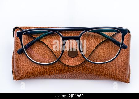 Brille mit schwarzem Rahmen aus Acetat-Material, die auf einem braunen Lederetui auf weißem Hintergrund aufliegt Stockfoto