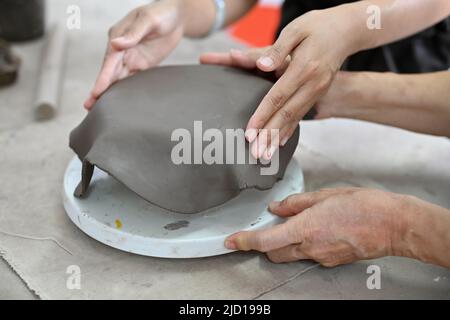 Professionelle gealterte Lehrerin hilft einer schönen jungen Frau, Tontöpfe in der Werkstatt zu machen. Zugeschnittenes Bild Stockfoto