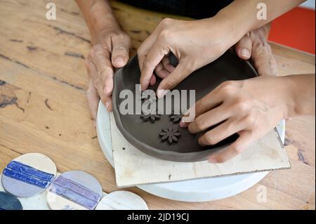 Draufsicht Bild, Hände machen eine Ton-Keramik, Dekoration einer Tonplatte auf Arbeitstisch in der Werkstatt. Handgemachte Töpferei Konzept Stockfoto