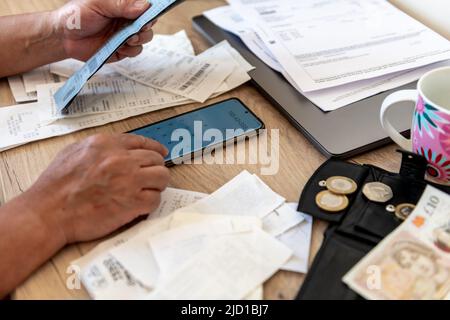 Eine Person, die die Lebenshaltungskosten mit einem Telefonrechner und einem Schreibtisch mit Rechnungen und Kassenbelegen berechnet. Stockfoto