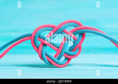 Herzförmiger keltischer Knoten aus zwei geflochtenen geflochtenen Schnüren auf blauem Hintergrund. Lebenszyklus-Konzept. Stockfoto